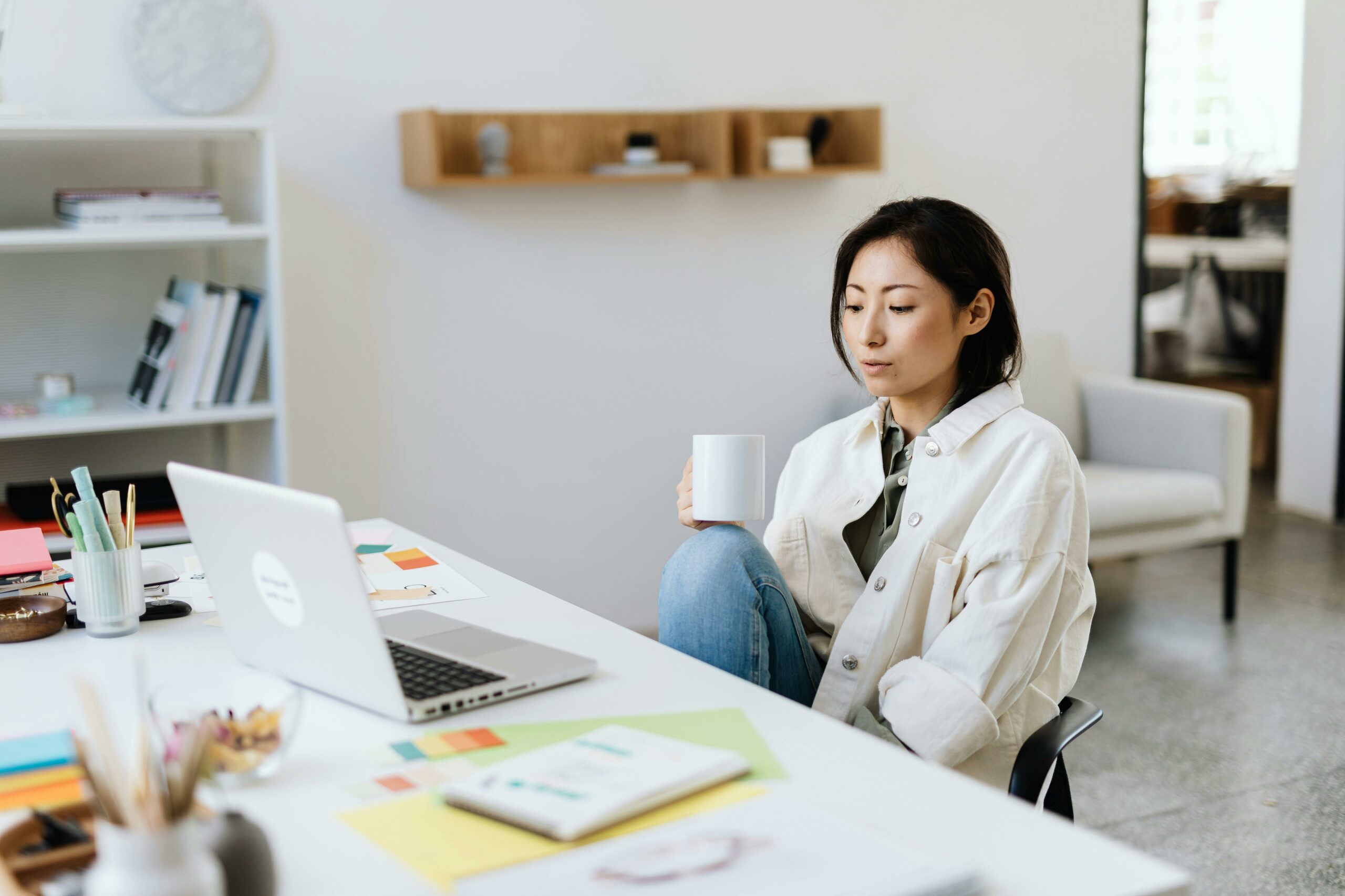 raveler working remotely with a cup of coffee at a desk, exploring side hustles for travelers using a laptop in a minimalist home office.